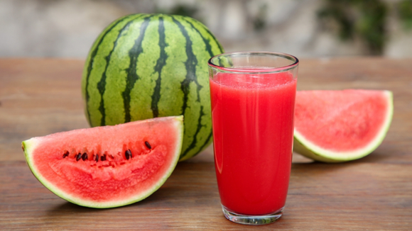 Suco de melancia vermelhinho em copo grande com fatias da fruta ao lado (Créditos: Shutterstock)