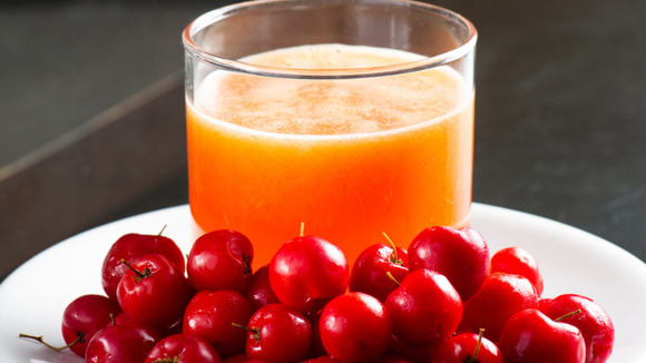 Copo de suco de acerola em cima de prato branco com as frutas (Créditos: Shutterstock)