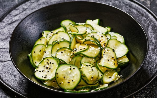 Sunomono com finas fatias de pepino e gergelim no prato preto
