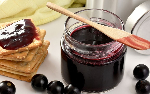 Geleia de jabuticaba no pote aberto com torrada e a fruta do lado