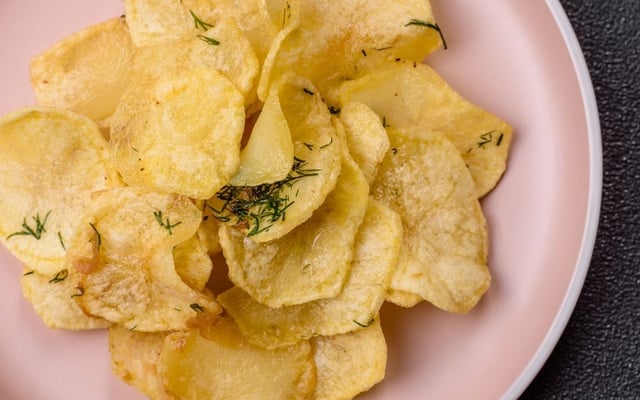 Batata chips na airfryer em um prato rosa com ervas por cima