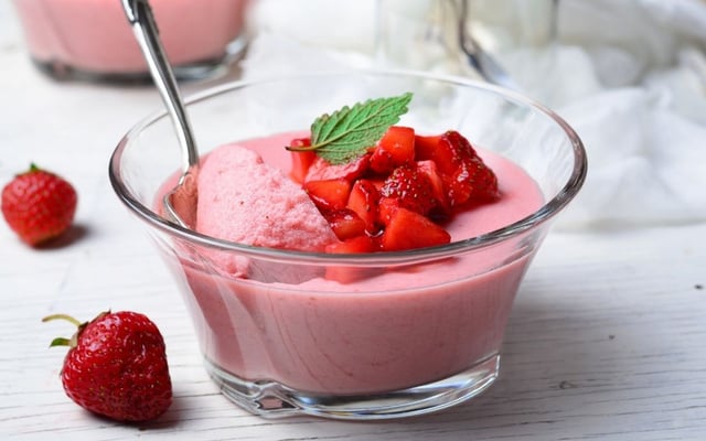 Gelatina cremosa servida em copo com morangos picados