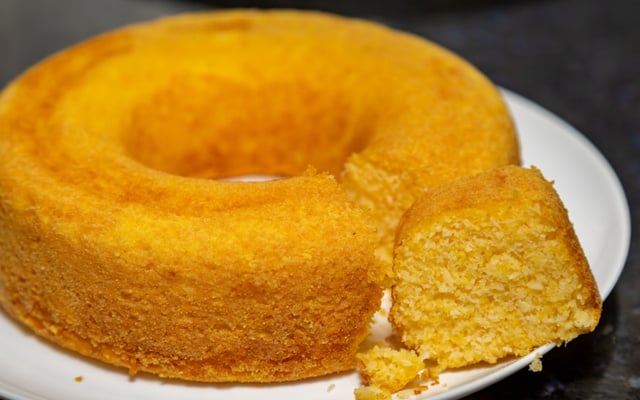 Bolo de fubá cremoso redondo com fatia cortada em prato branco