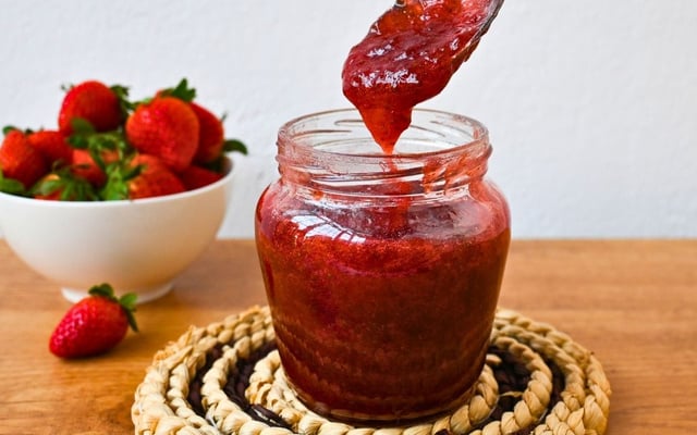 Geleia de morango caseira em pote com a fruta atrás