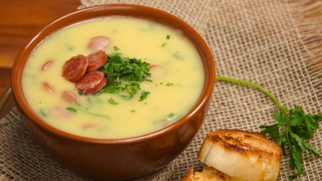 Tigela com caldo cremoso de mandioquinha servido com linguiça defumada fatiada e cheiro-verde (Créditos: TudoGostoso)