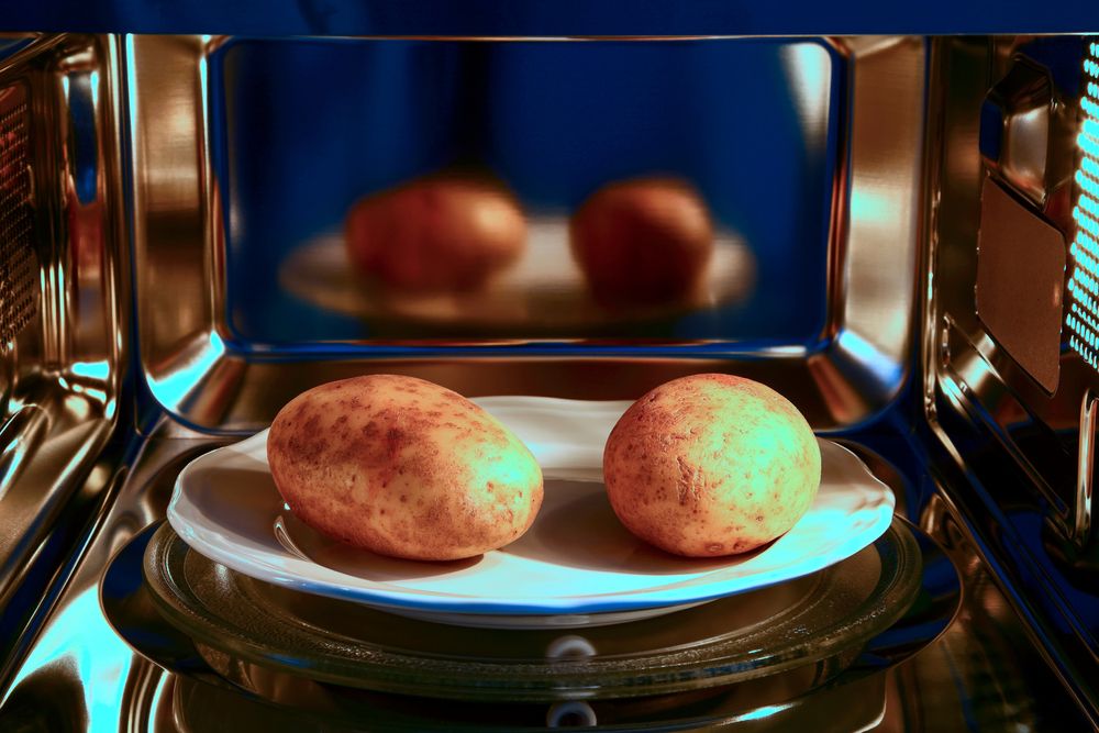 duas batatas inteiras dentro de um prato, no micro-ondas, mostrando como cozinhar batata no micro-ondas