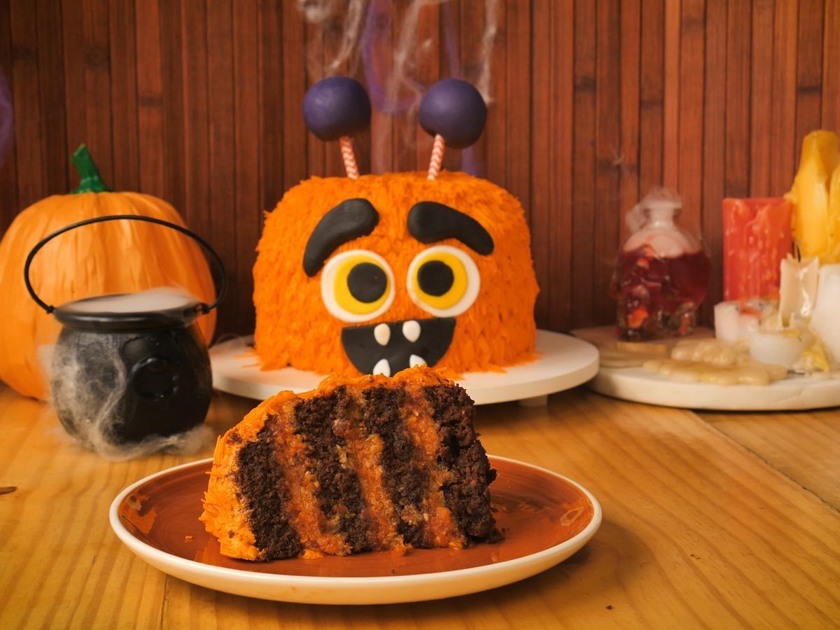 Uma mesa decorada com comida halloween. Um prato com uma fatia de bolo de abóbora