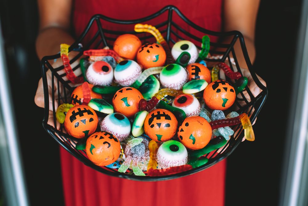 Pessoa segurando vasília com doces de halloween em formato de abóbora, olho e minhoca de gelatina