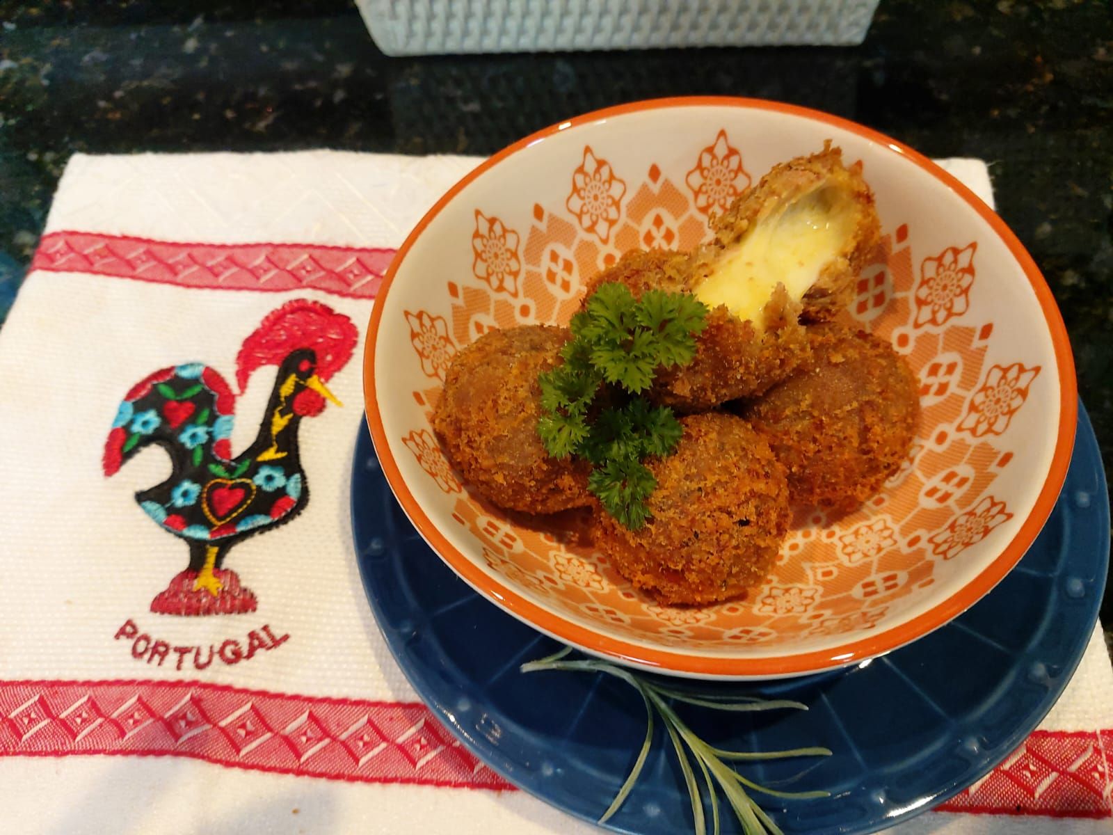 Portugal Fest: cinco bolinhos de alheira com queijo em um bowl com desenhos laranjas em uma toalha com galo e Portugal bordado