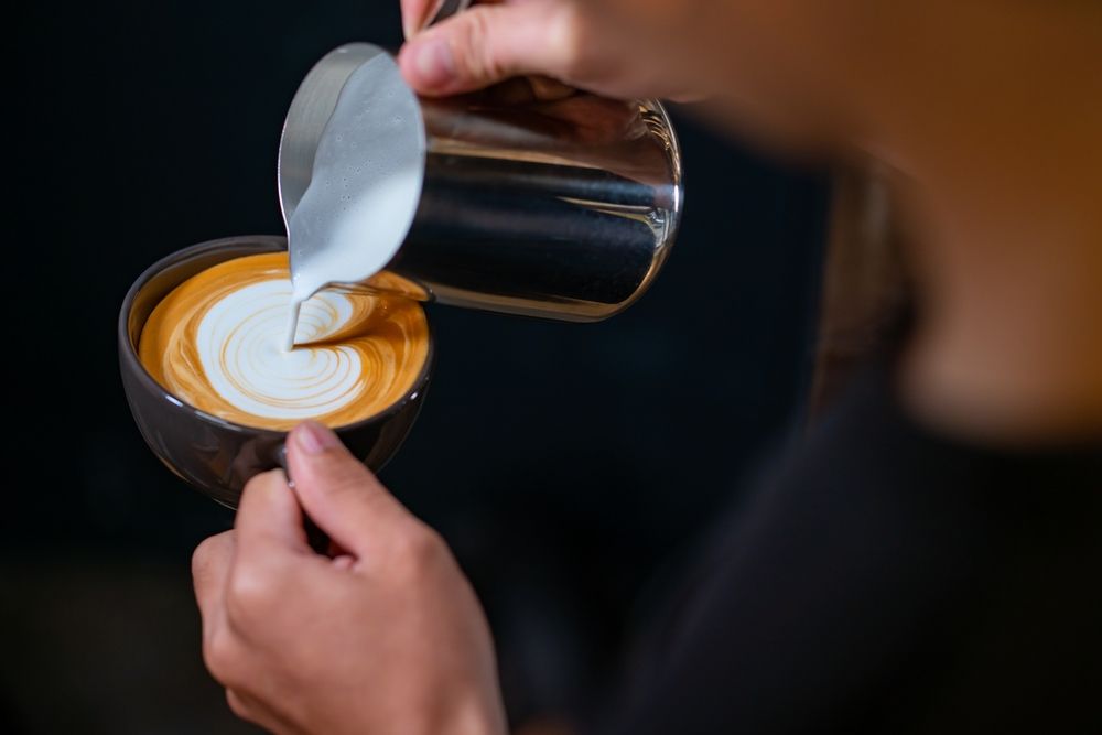 Como fazer cappuccino: uma pessoa colocando leite com espuma no café expresso