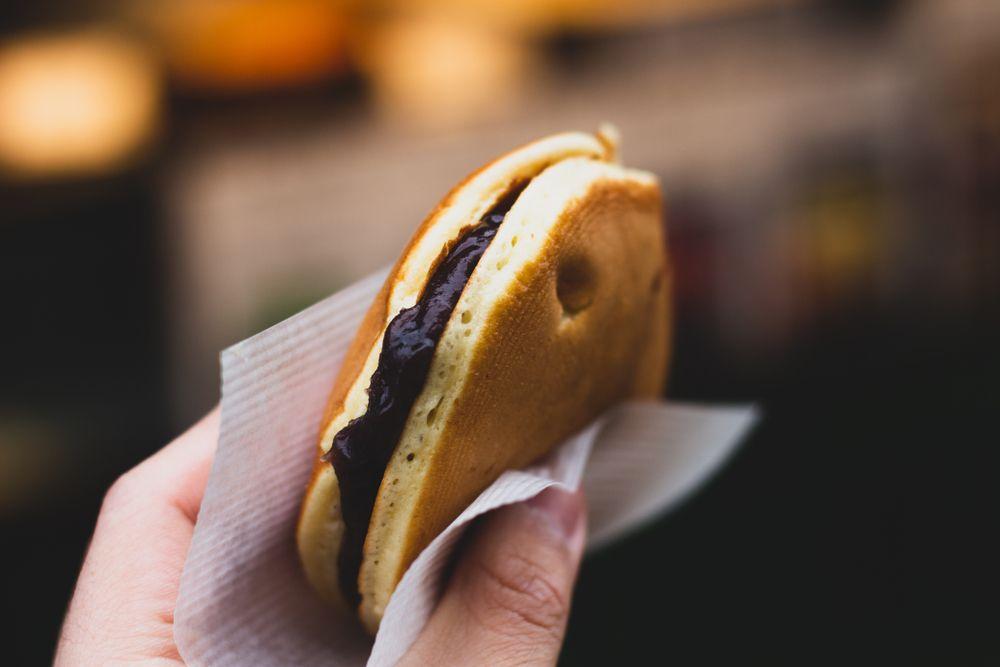 Close de uma mão segurando um dorayaki, doce japonês, com auxílio de um guardanapo
