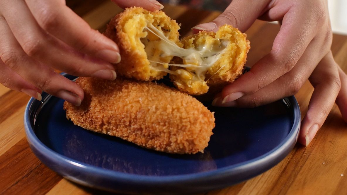 Farinha panko: palitinho crocante de milho e queijo no prato e sendo aberto com as mãos