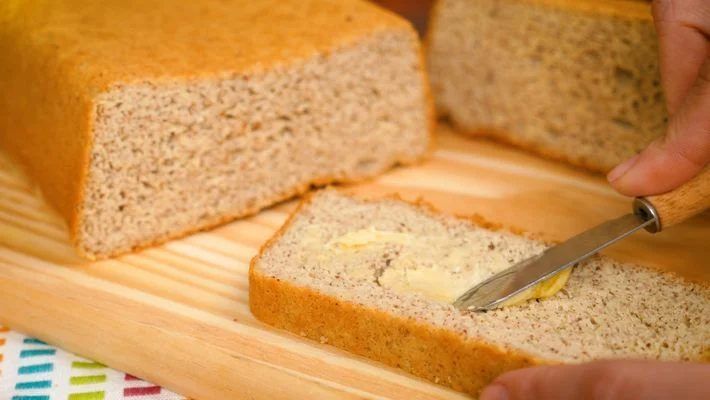 Receitas low carb: pão low carb com uma fatia na frente e pessoa passando manteiga