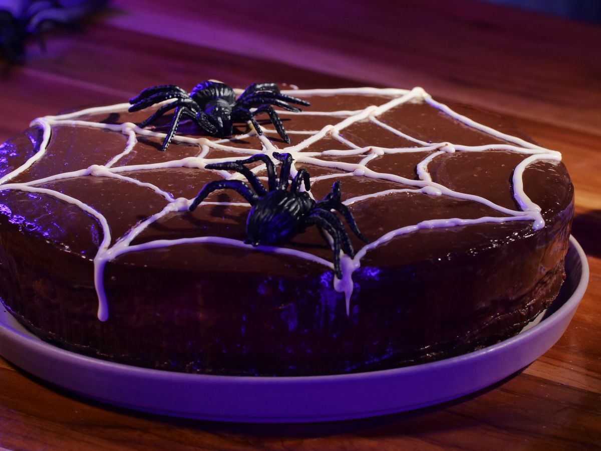 Um bolo com decoração de teia em branco, com algumas teias de plástico por cima, bem comida de halloween.