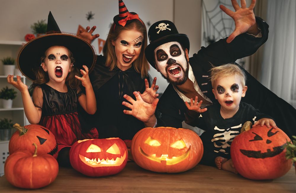 Família com fantasias de halloween fazendo expressões assustadoras com abóboras com rosto na mesa