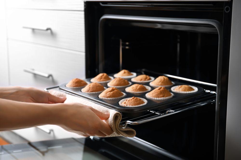 Pessoa retirando uma fornada de 12 cupcakes do forno