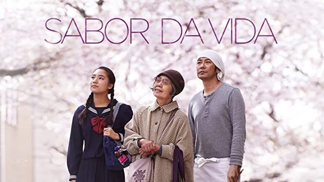 3 personagens principais do filme Sabor da Vida (uma estudante, uma idosa e um cozinheiro) à frente de uma cerejeira florida, o título do filme acima deles