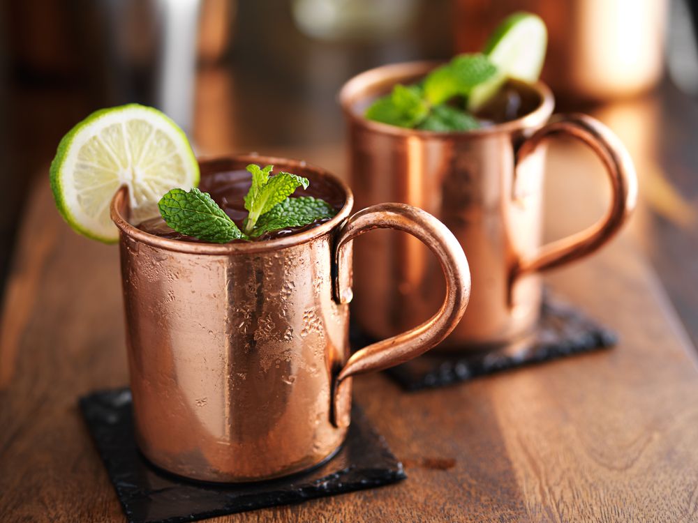 duas canecas de cobre de Moscow Mule em cima de uma mesa de madeira