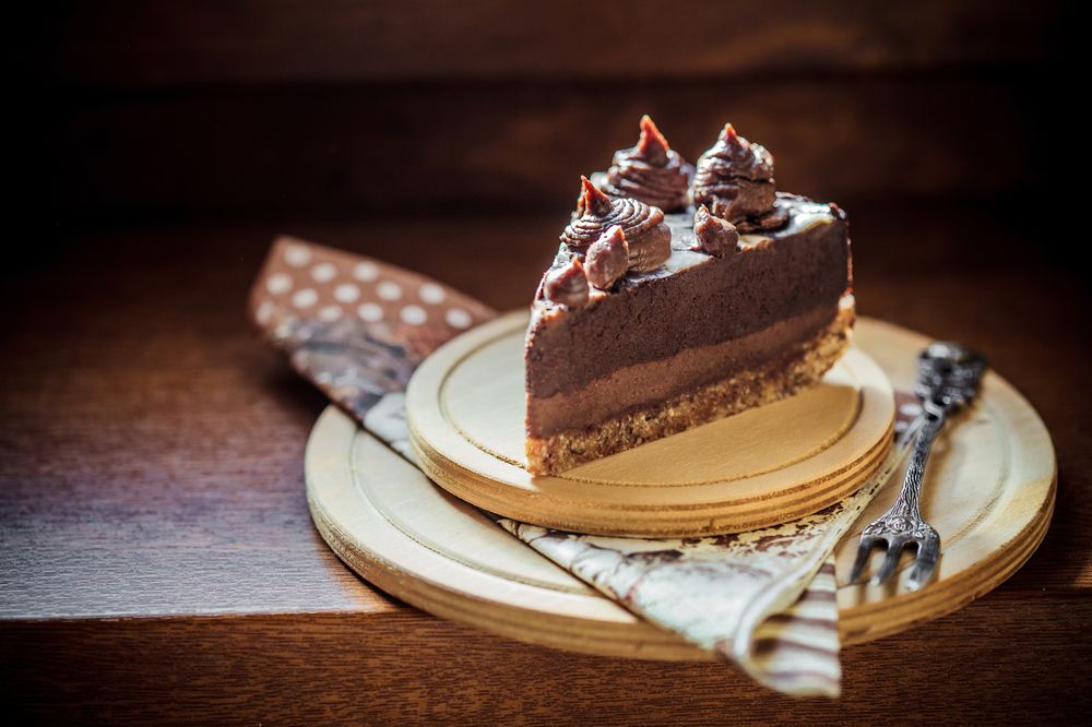 Fatia de bolo de mousse chocolate confeitado com suspiros e sobre tábuas de madeira com um garfo de estilo antigo e um guardanapo marrom com bolinhas
