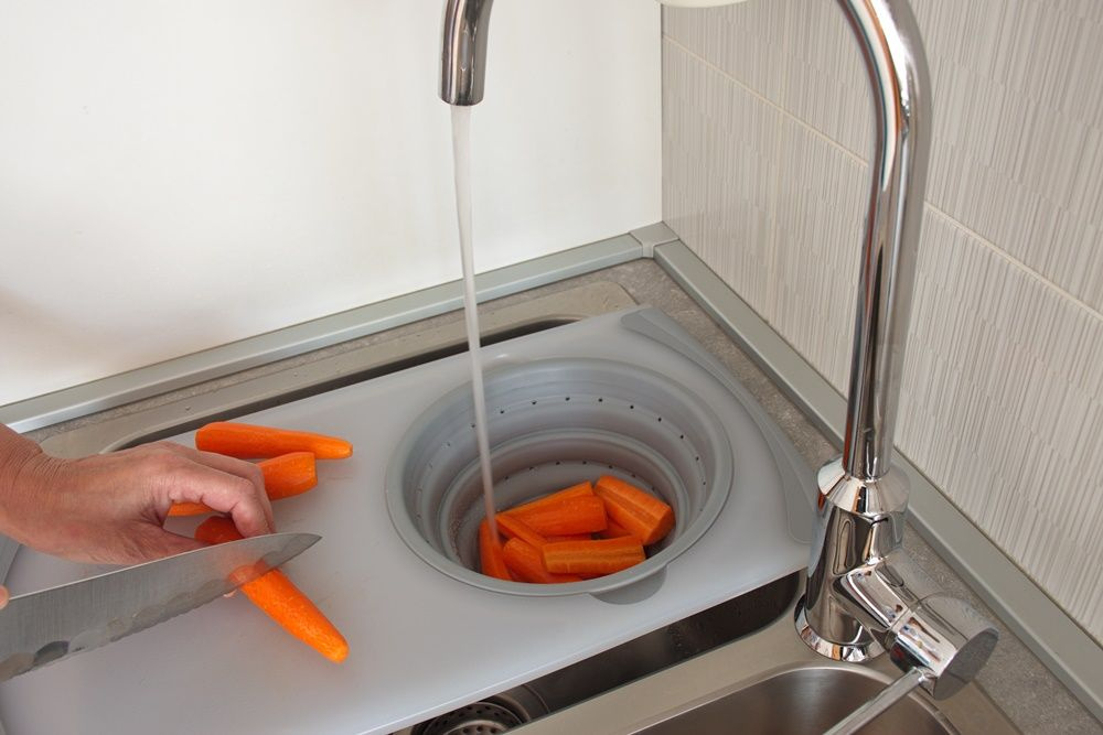 Tábua de cortar legumes encaixada em cima de uma pia